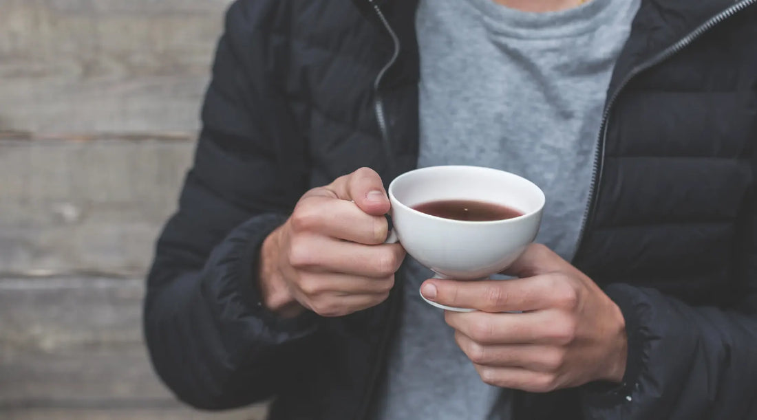 Cropped shot of a man wearing a black coat holding a white teacup