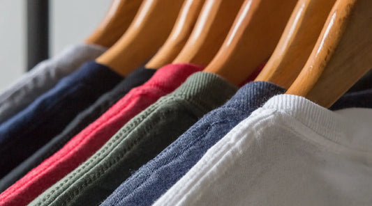 A row of wooden hangers holding various colored t-shirts neatly lined up in a closet.