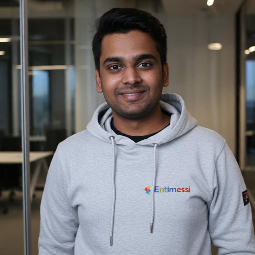 A young man, dressed in a custom grey hoodie, stands confidently in a corporate office setting