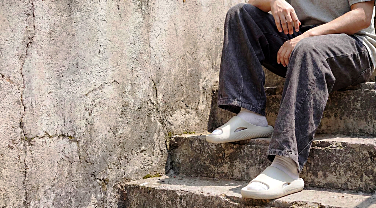 Man sitting on stone steps wearing bone-white recovery slides with white socks